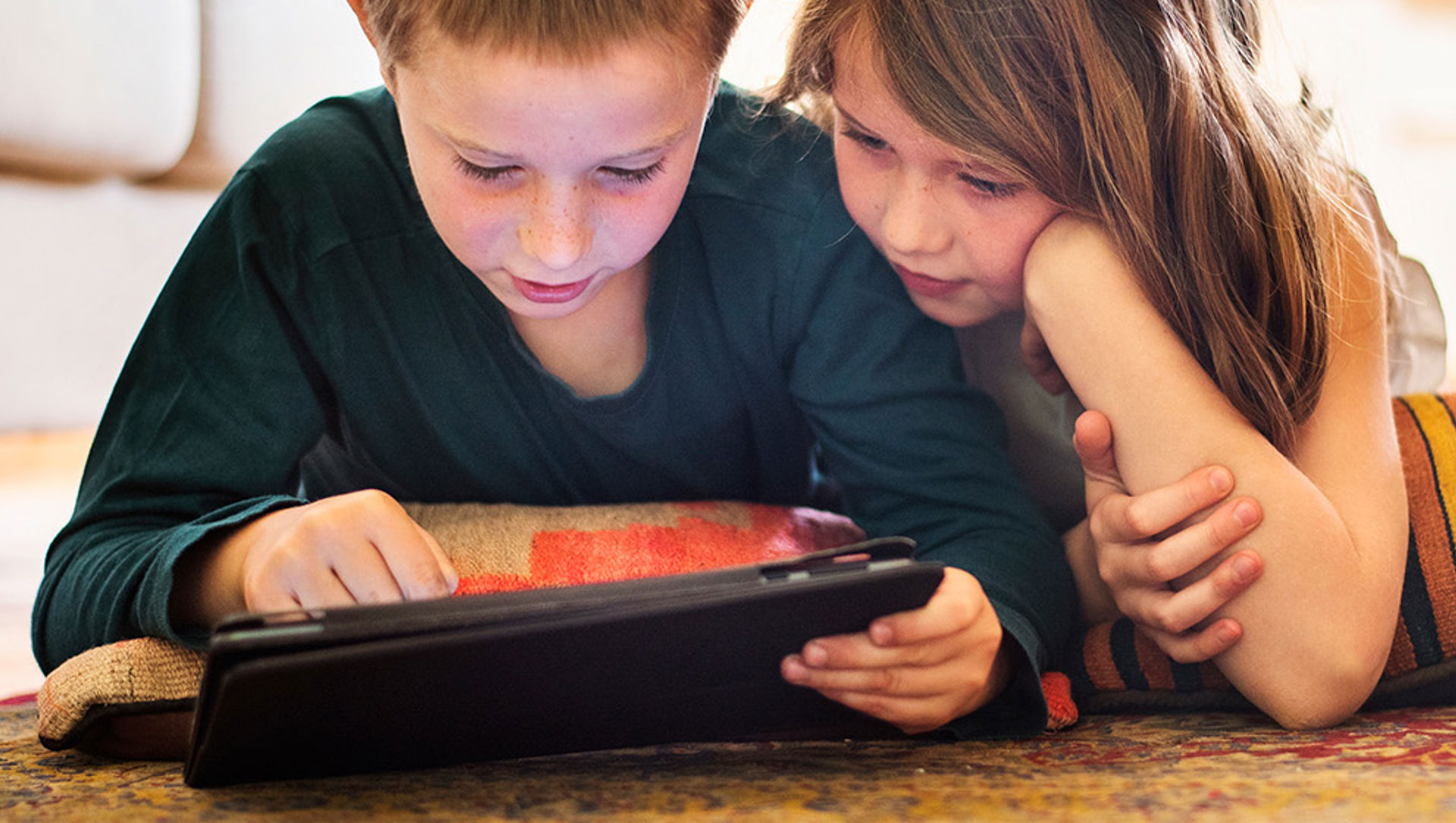 Brother and sister using tablet on living room floor