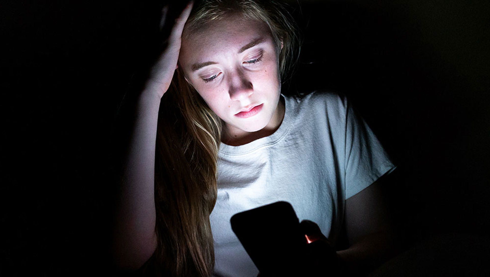 An unhappy girl using her mobile phone in a dark room