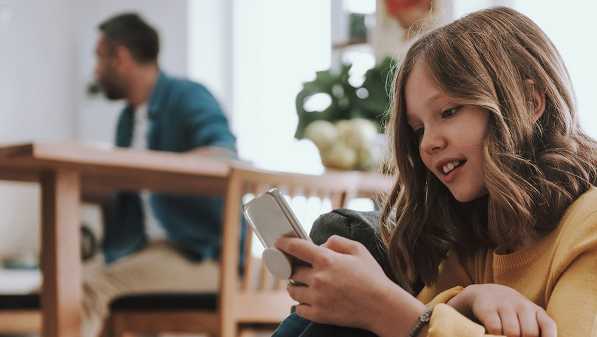 A girl happily looking at a mobile phone in a home environment