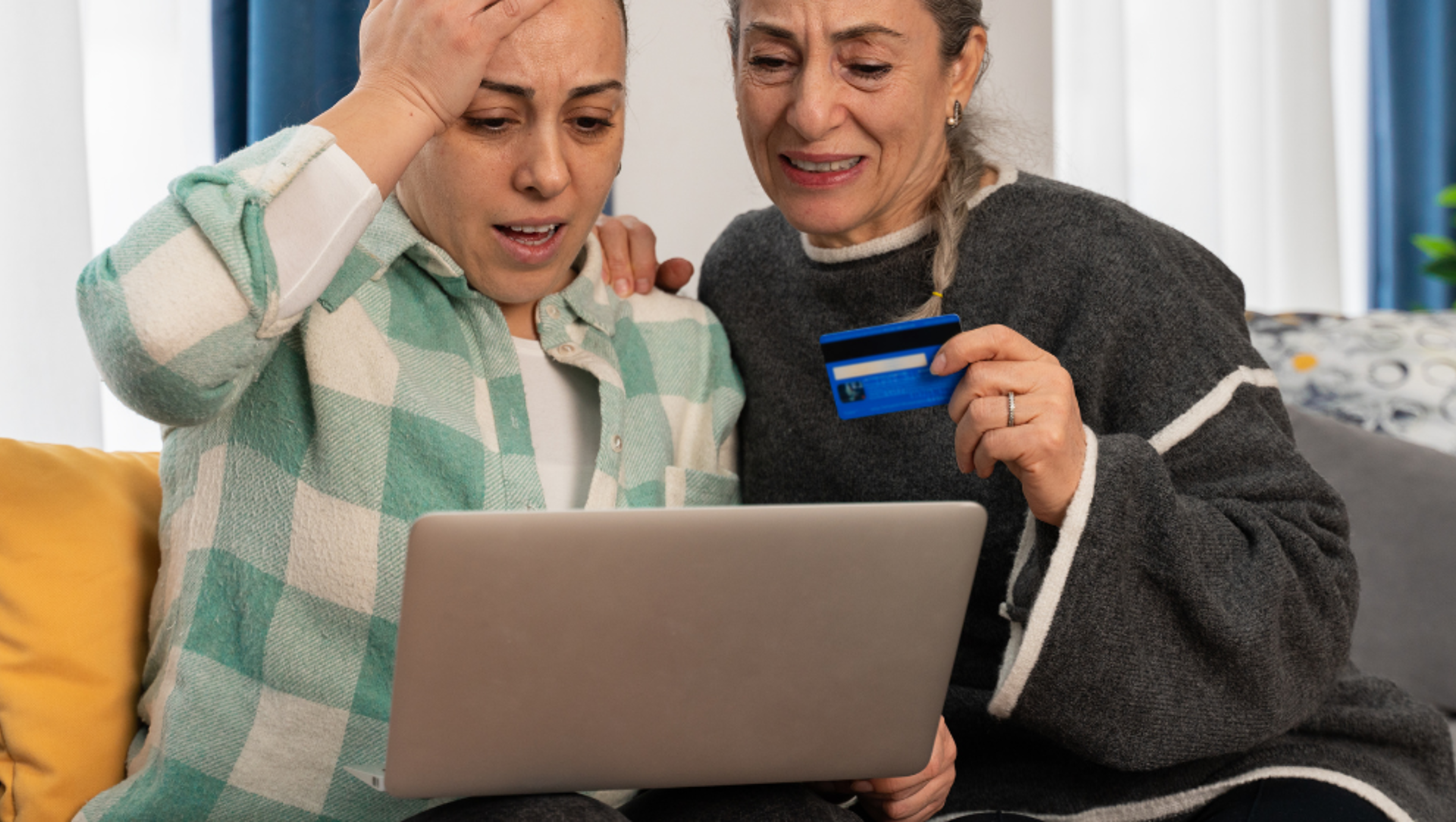 Two distressed women using a laptop with a credit card in hand