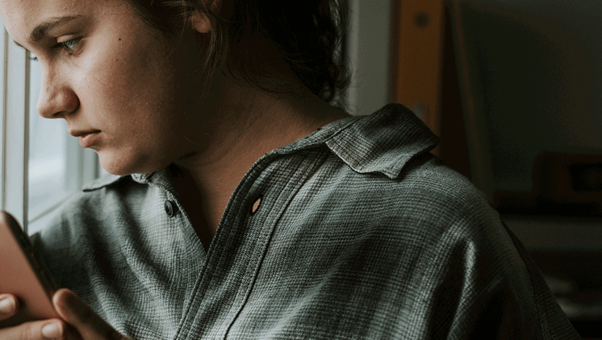 Young, sad-looking girl on phone looking out of window