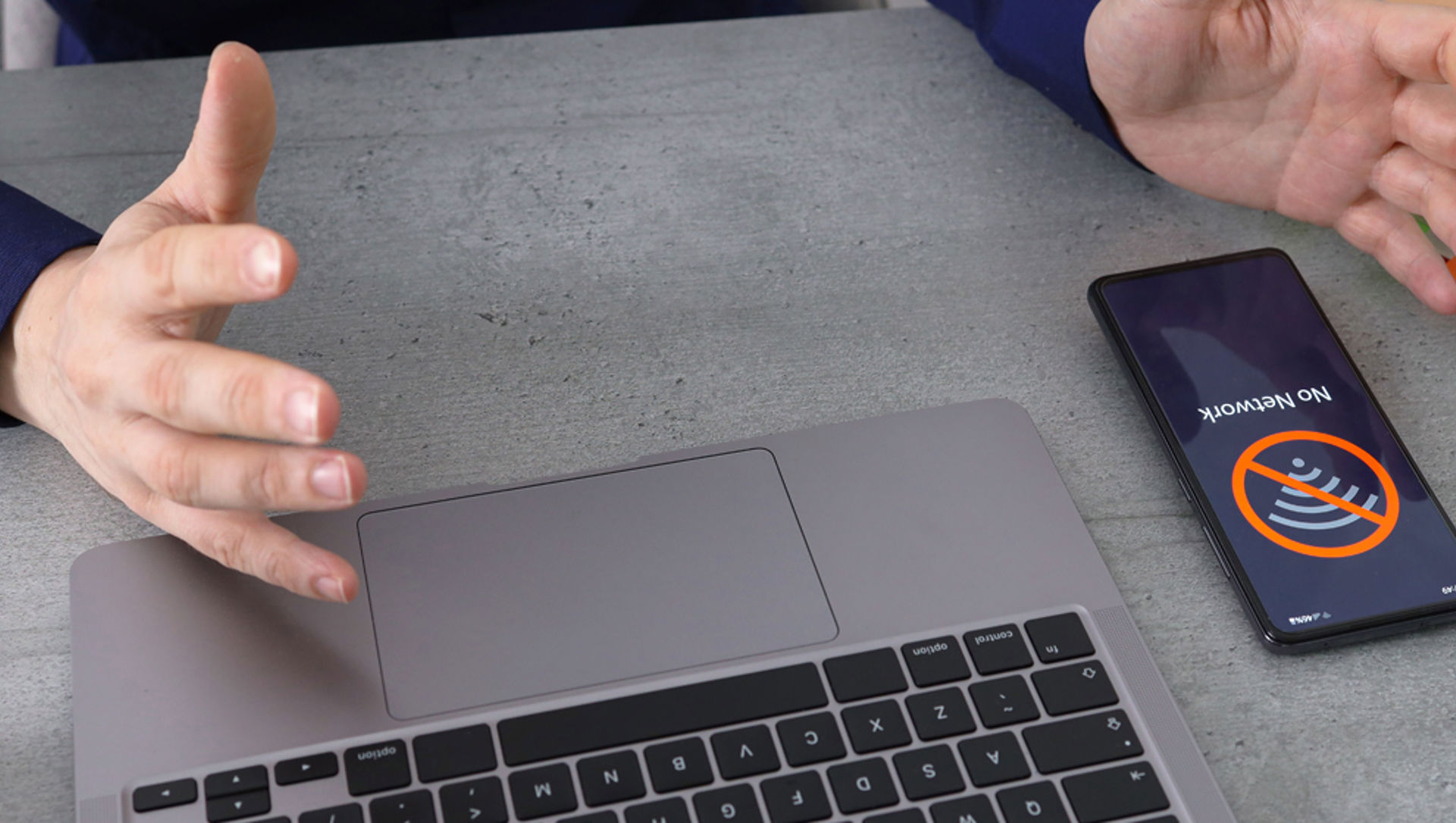 A person working at a laptop with a mobile phone next to it and a 'no network' message on screen