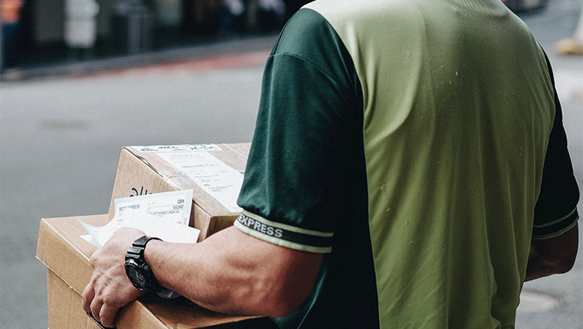 man in a green shirt carrying parcels through a quite street in a town